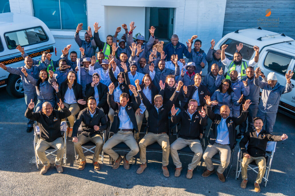 Sherwood Construction team group photo outside office in Cape Town with staff, builders, and project managers celebrating together beside company vehicles.
